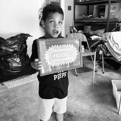 Boy looking up holding frame with text while standing in storage room