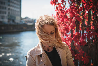 Close-up of young woman with tousled hair standing by river in city