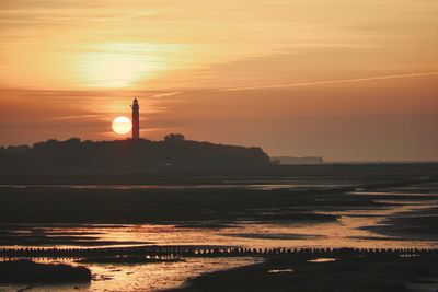 Silhouette lighthouse by sea against sky during sunset