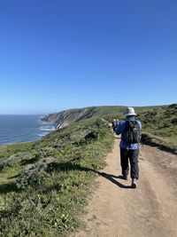Rear view of man photographing sea against clear sky