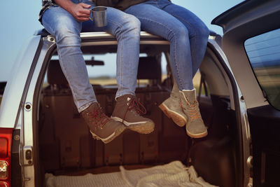 Low section of couple sitting on car roof