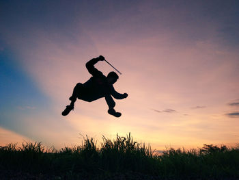 Silhouette man jumping on field against sky during sunset