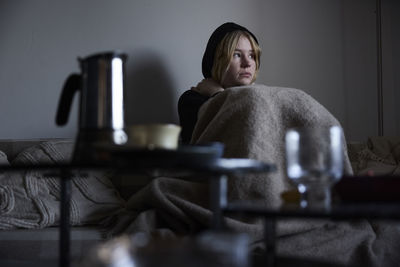 Teenage girl sitting on sofa wrapped in blanket