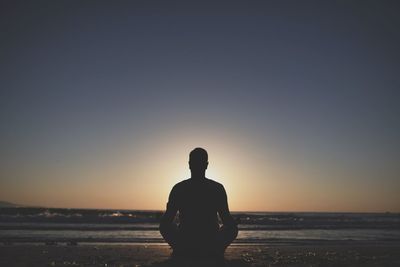 Young man in meditation near the sea. concept of pray. adult practice yoga on the beach at sunset.