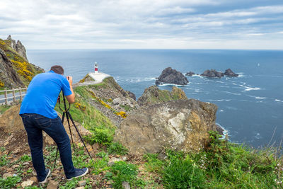 Rear view full length of man photographing sea while standing on rock