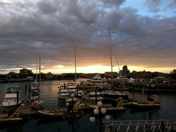 Boats moored at harbor against cloudy sky during sunset