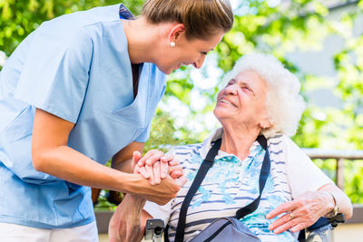 Nurse helping woman sitting against trees