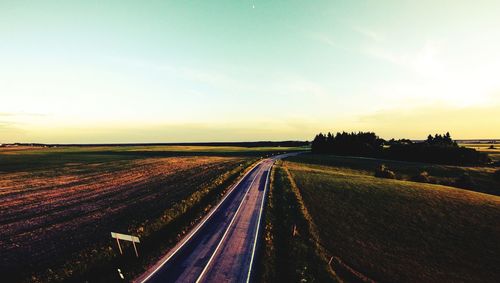 Road amidst field against sky during sunset