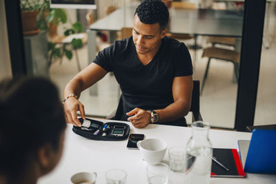 Businessman doing blood test while sitting with colleague at table