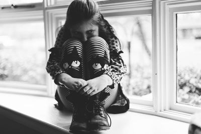 Close-up of girl hugging knees while sitting on window sill