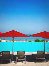 Lounge chairs by swimming pool at beach against clear blue sky