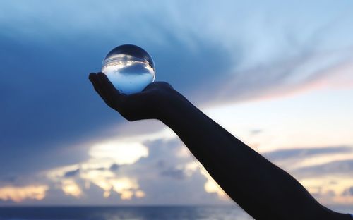 Low angle view of silhouette hand holding crystal ball against sky
