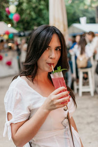 Beautiful young woman drinking strawberry mojito cocktail in park in city