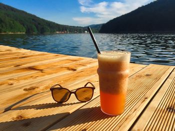 Glass of orange smoothie with drinking straw with a pair of sunglasses on a rustic wooden pontoon