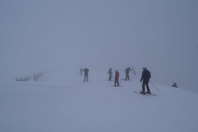 People skiing on snow covered land against sky