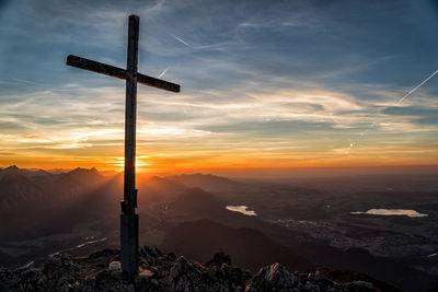 Cross on landscape against sky during sunset