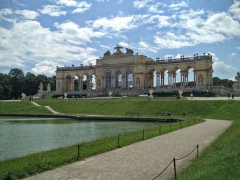 Schonbrunn palace in front of river against sky on sunny day