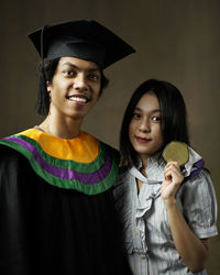 Portrait of friends wearing graduation gown and medal
