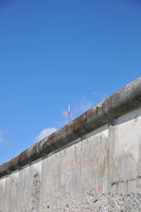 Low angle view of birds on wall against clear blue sky