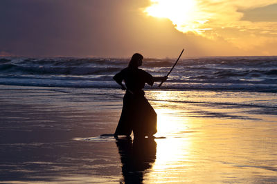 Young samurai women with japanese sword katana  at sunset on the beach