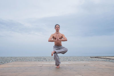 Full length of shirtless man standing at beach against sky