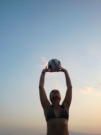 Young woman in bikini playing beach volleyball against sky