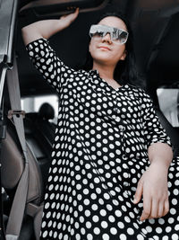 A girl wearing a polkadot dress, sun glasses and high boots sitting in a car 