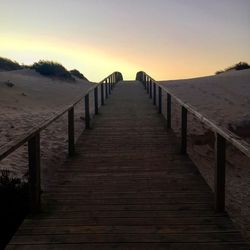 Boardwalk on beach against clear sky during sunset