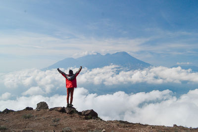 Rear view of female hiker with arms raised standing on mountain peak against sky