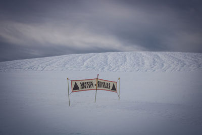 Information sign on snow covered landscape against sky