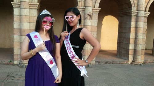 Portrait of smiling females with props while standing against building