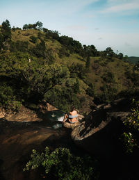 People sitting on riverbank by tree mountain