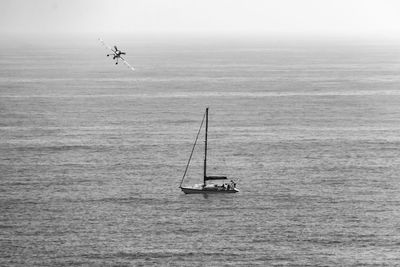 Sailboat in sea against sky and airplane flying in the sky. 