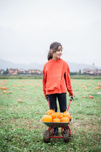 Girl in orange hoodie with pumkins standing on a field