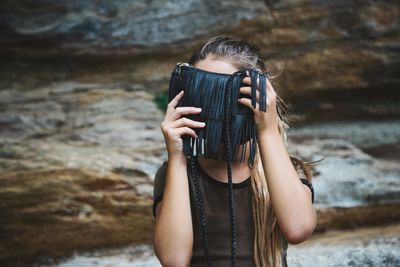 Close-up of woman hiding face behind purse against rock formation