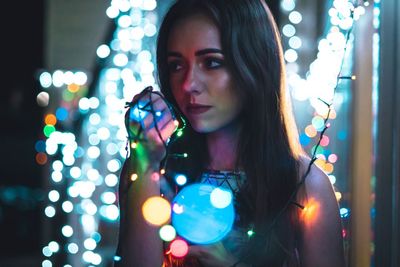 Young woman holding illuminated string lights at night