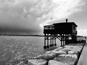 Stilt house by lake against cloudy sky