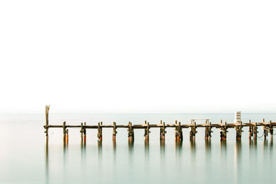 Wooden posts in sea against clear sky