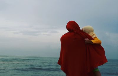 Rear view of woman with daughter while standing by sea against sky