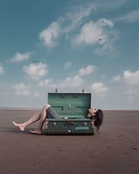 Full length of woman lying down in suitcase at beach