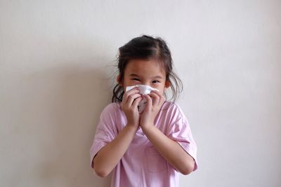 Portrait of cute girl holding face against wall