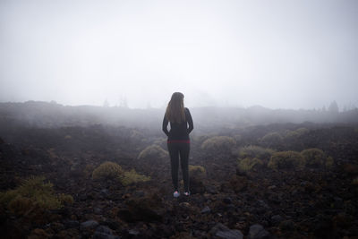 Rear view of woman standing on mountain against sky