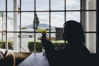 Side view of woman holding flower while sitting in restaurant