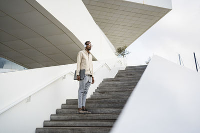 Man standing with laptop wearing headphones on staircase