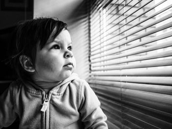 Close-up of baby girl looking through window at home