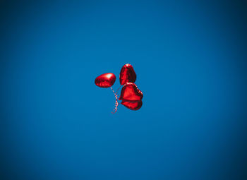 Low angle view of red balloons flying against blue sky