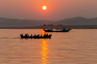 Silhouette people on boat in sea against orange sky