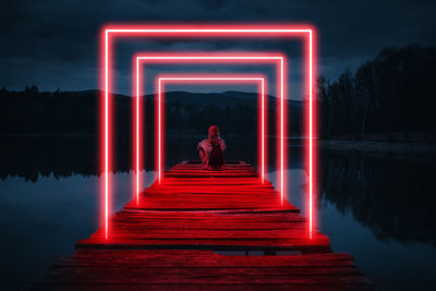 Man sitting on illuminated pier over lake at night