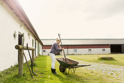 Female farmer removing work tools from wheelbarrow at farm