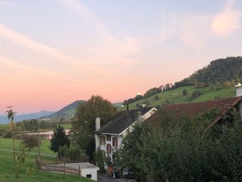 Houses by trees and buildings against sky during sunset